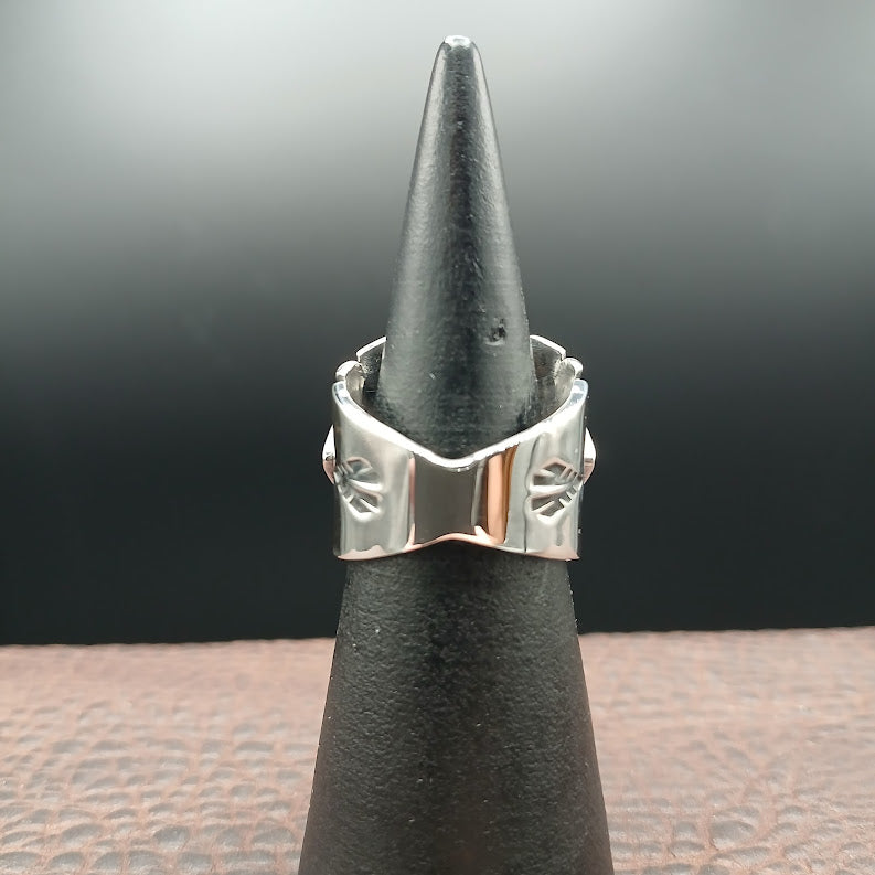 Silver ring with a pointed design on a black stand against a dark background