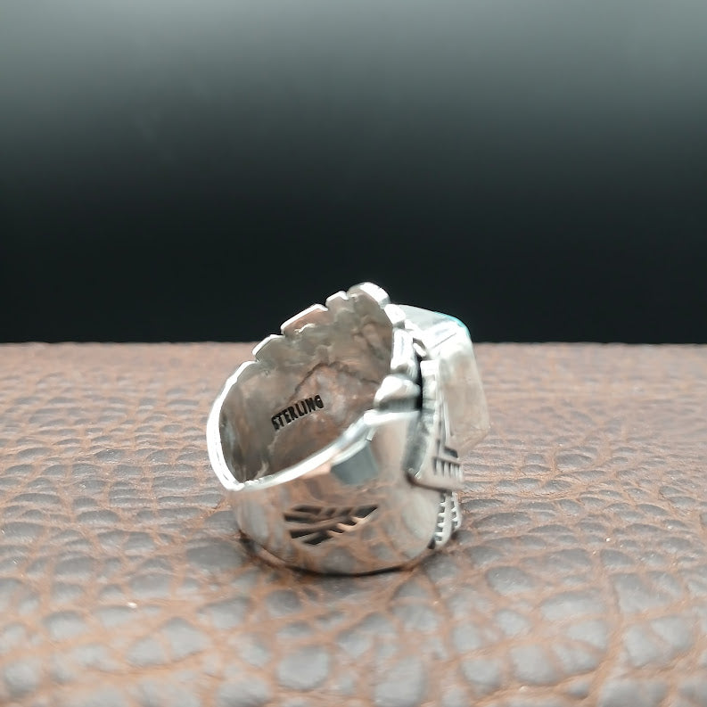 Silver ring with intricate design on a textured surface