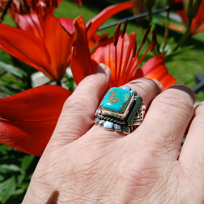 Hand wearing a ring with a turquoise stone against a red flower background