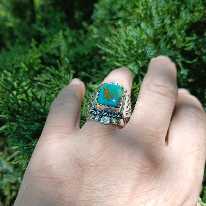 Hand wearing a turquoise ring with a green juniper background