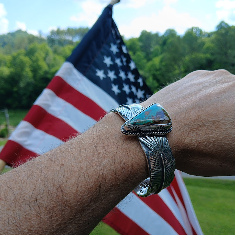 Silver bracelet with a turquoise stone on a wrist in front of an American flag.