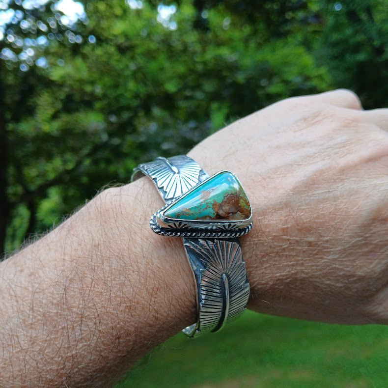 Silver bracelet with a turquoise stone on a wrist against a blurred green background