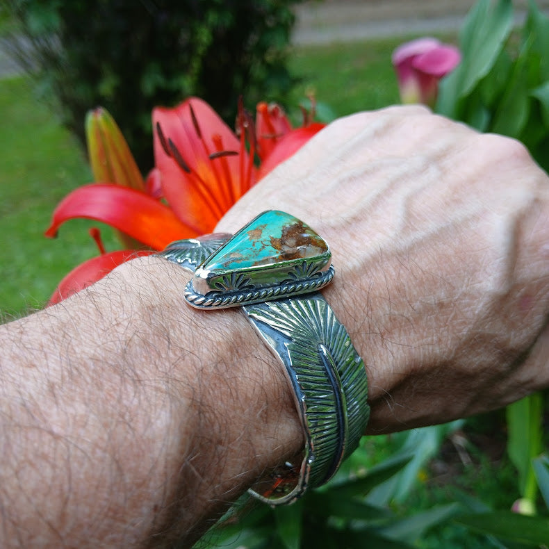 Hand wearing a silver and turquoise bracelet with flowers in the background