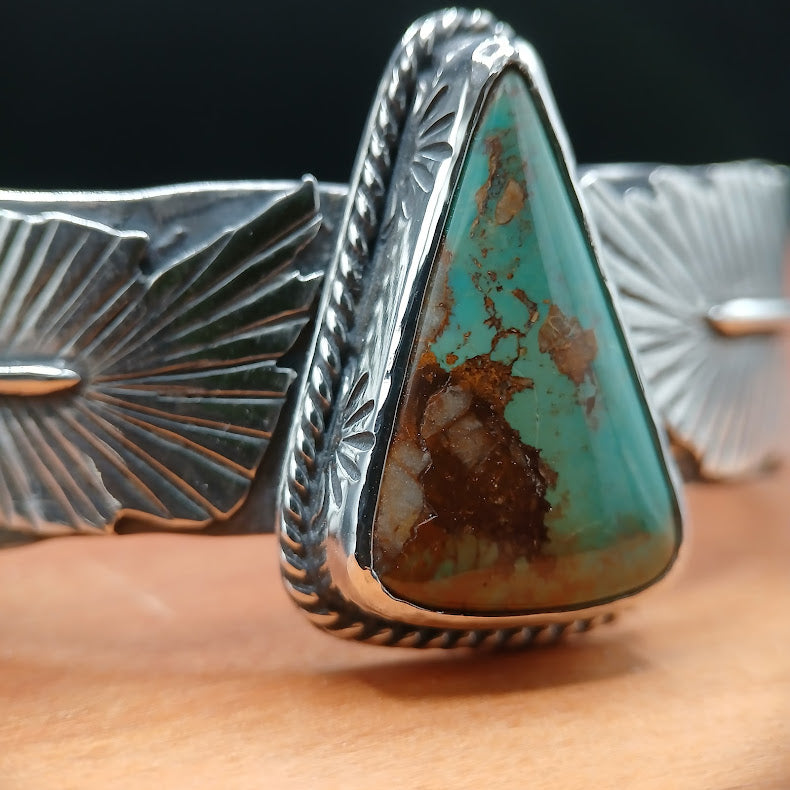 Silver ring with a triangular turquoise stone on a wooden surface