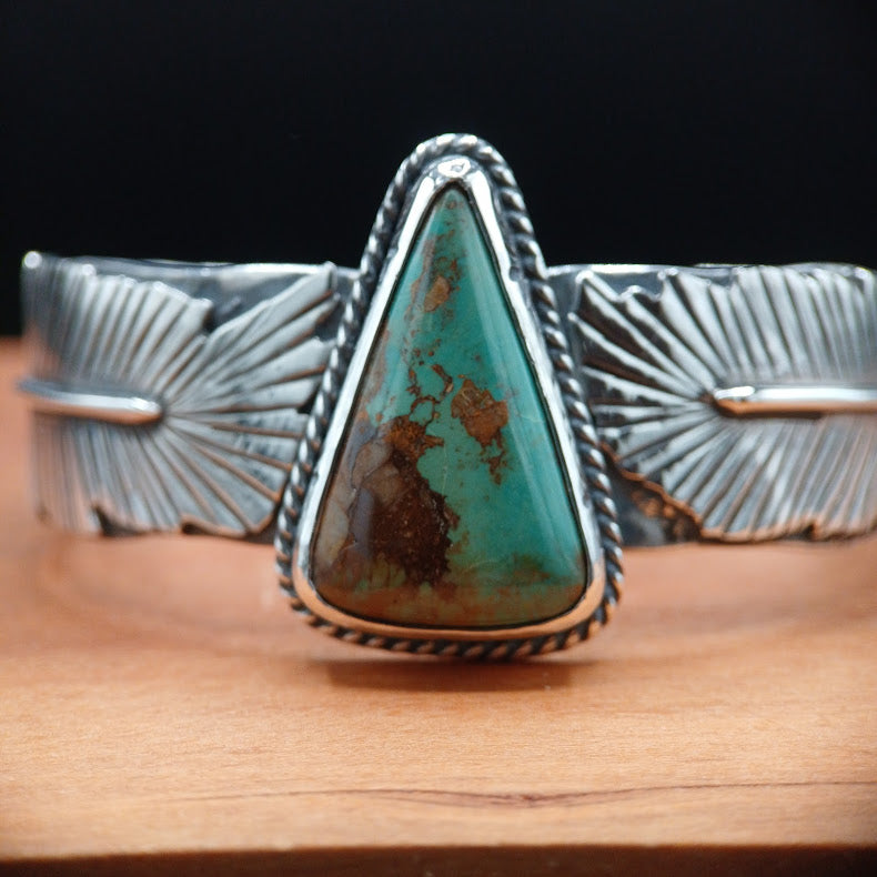 Silver bracelet with a large turquoise stone on a wooden surface