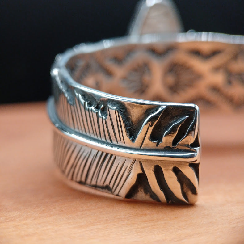 Silver feather-shaped ring on a wooden surface with a blurred background