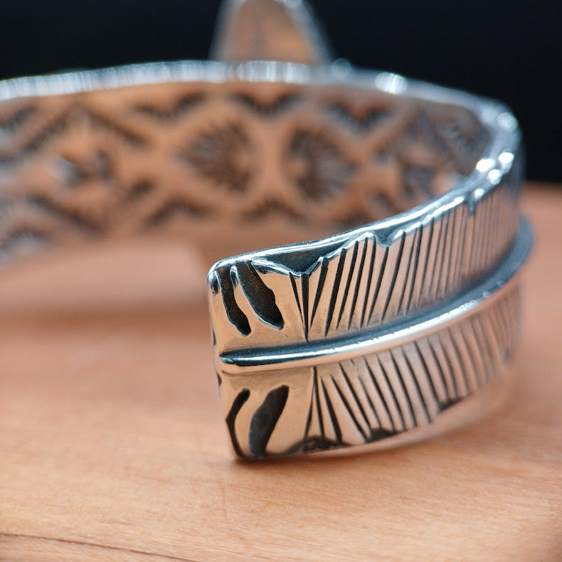 Silver feather-shaped bracelet on a wooden surface with a blurred background