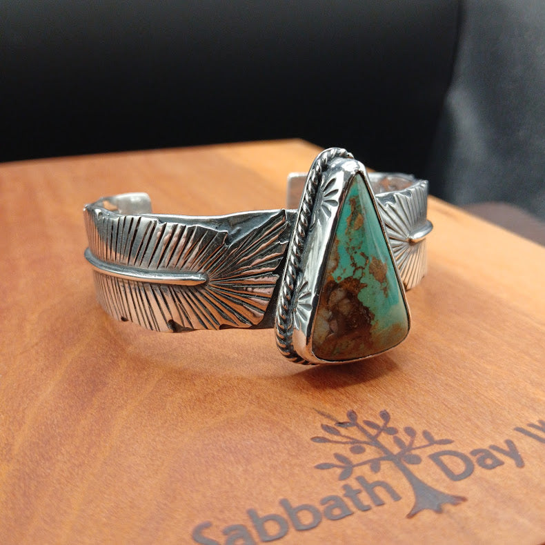 Silver cuff bracelet with a turquoise stone on a wooden surface.