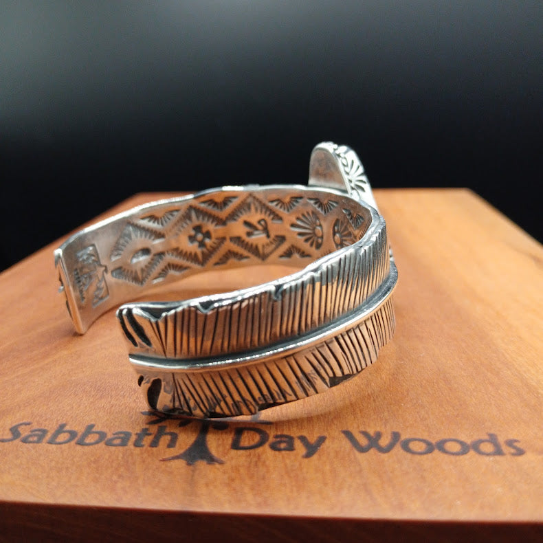 Silver bracelet with intricate designs on a wooden surface with 'Sabbath Day Woods' branding.