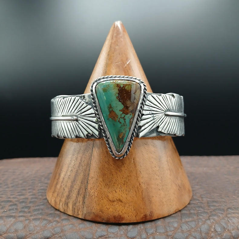 Silver bracelet with a turquoise stone on a wooden stand against a dark background