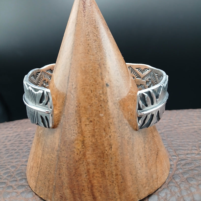 Silver rings with intricate designs on a wooden stand against a dark background
