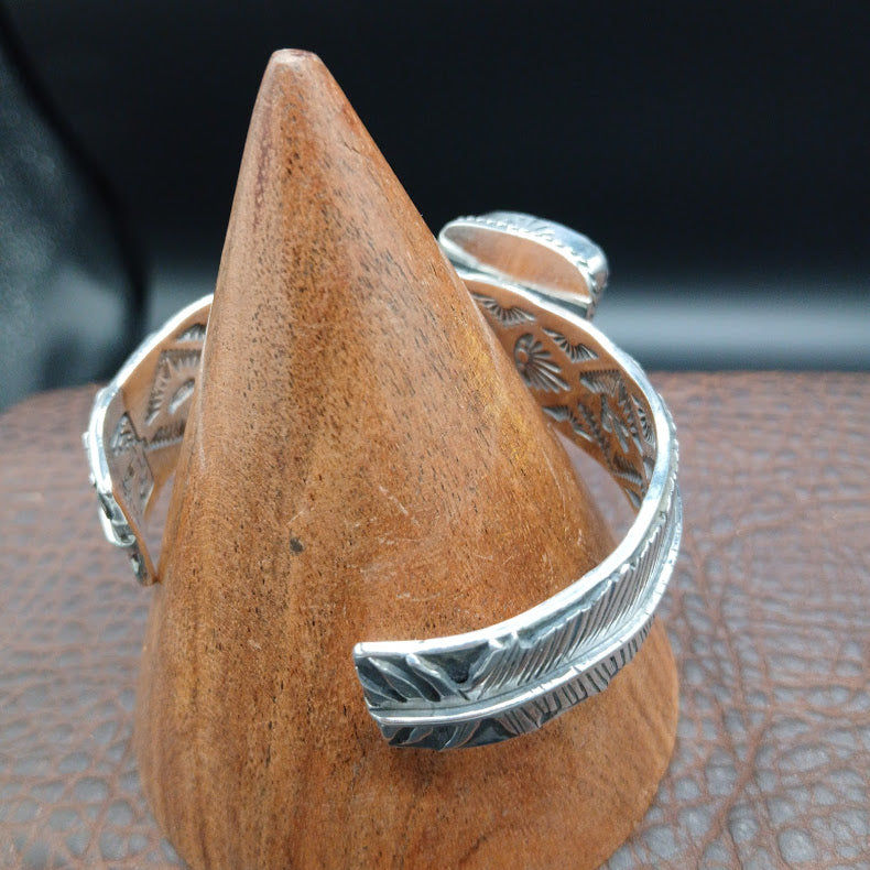 Silver bracelet with feather design on a wooden block