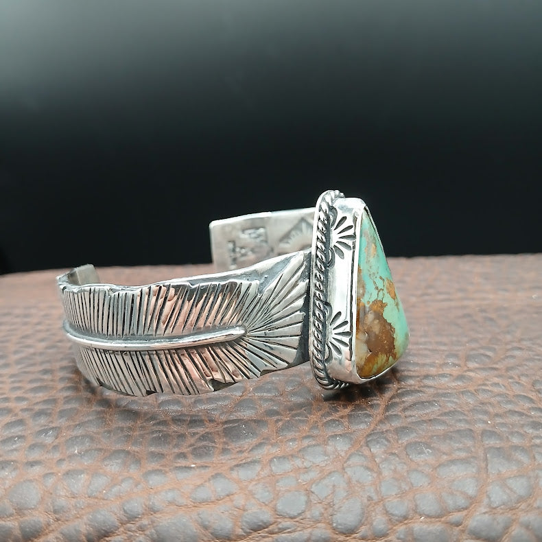 Silver feather-shaped bracelet with turquoise stone on a textured surface