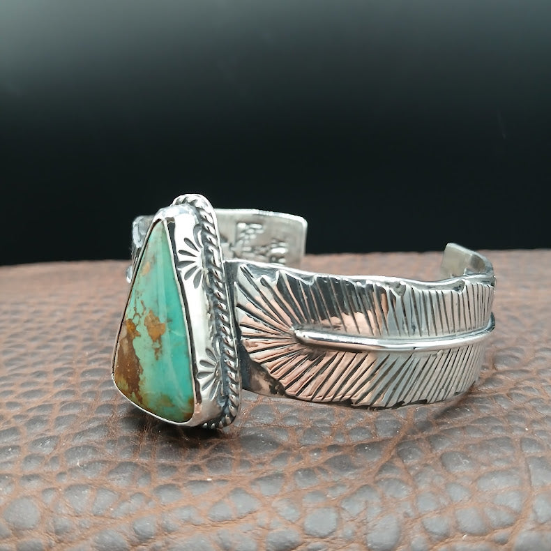 Silver cuff bracelet with turquoise stone on a textured surface
