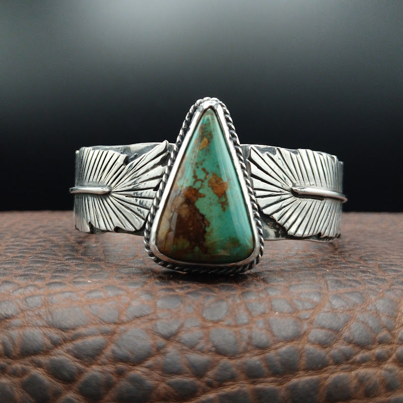 Silver cuff bracelet with a large turquoise stone on a textured surface