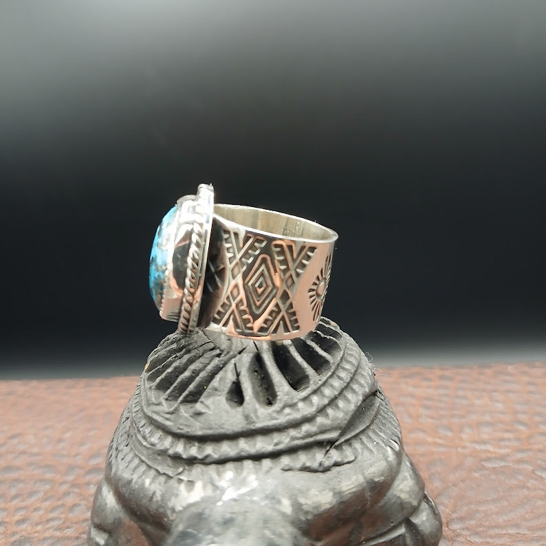 Silver ring with turquoise stone on a decorative metal stand against a dark background