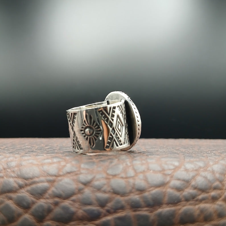 Silver ring with intricate designs on a textured surface