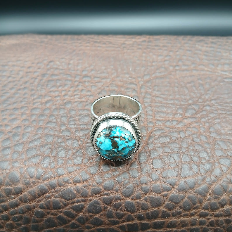 Silver ring with a turquoise stone on a brown leather surface