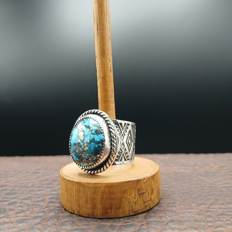 Silver ring with turquoise stone on a wooden stand against a dark background