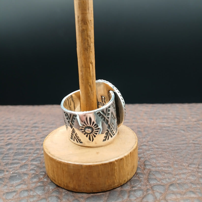 Silver ring with intricate design on a wooden stand against a dark background