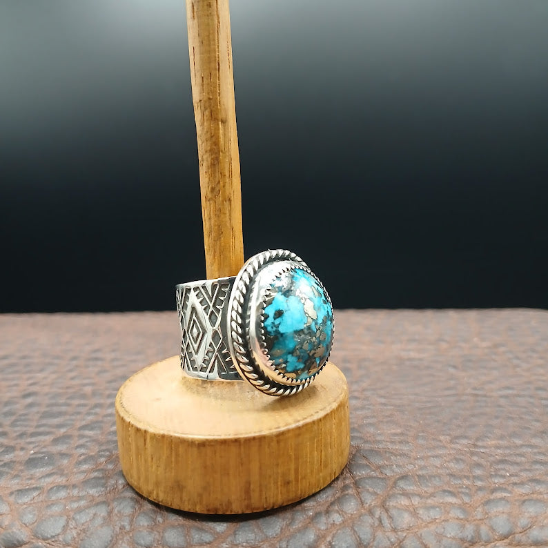 Silver ring with turquoise stone on a wooden stand against a dark background