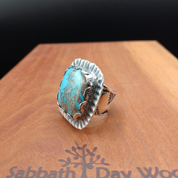 Natural turquoise and pyrite statement ring centered on dark background, serrated sterling silver bezel detail