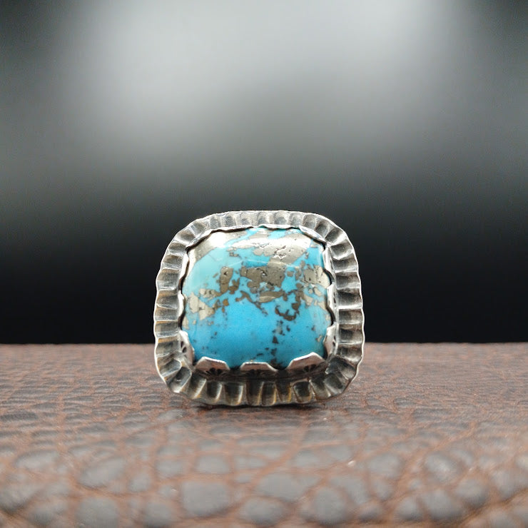 Back view of hand-stamped sterling silver ring shank showing geometric stampwork pattern, leather background