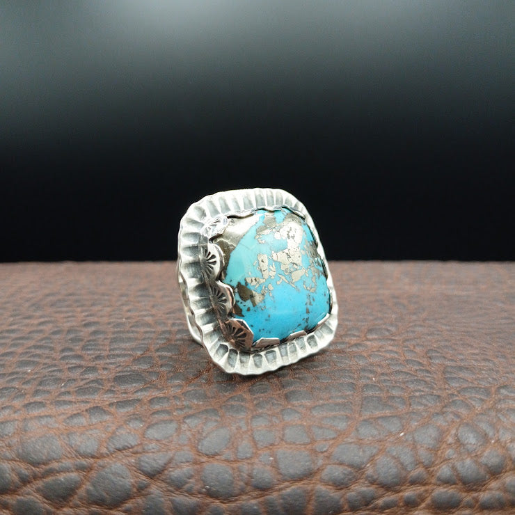 Three-quarter view of The Hardscrabble turquoise ring showing stamped concho details on bezel sides, dark background